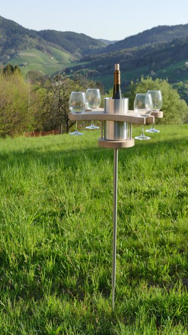 Ein Weinglas-Ständer mit Sektflasche und Gläsern in einer grünen Landschaft.